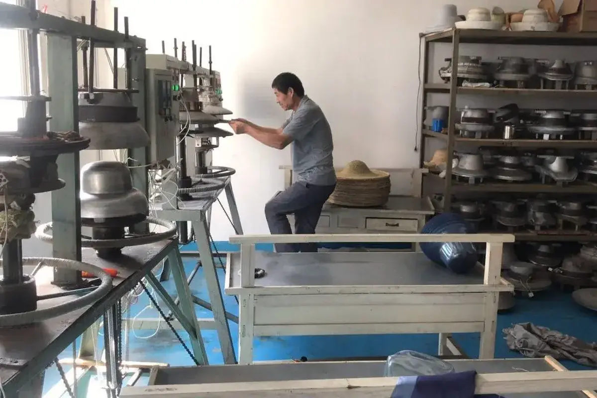 Factory worker shaping straw hat bodies with production equipment