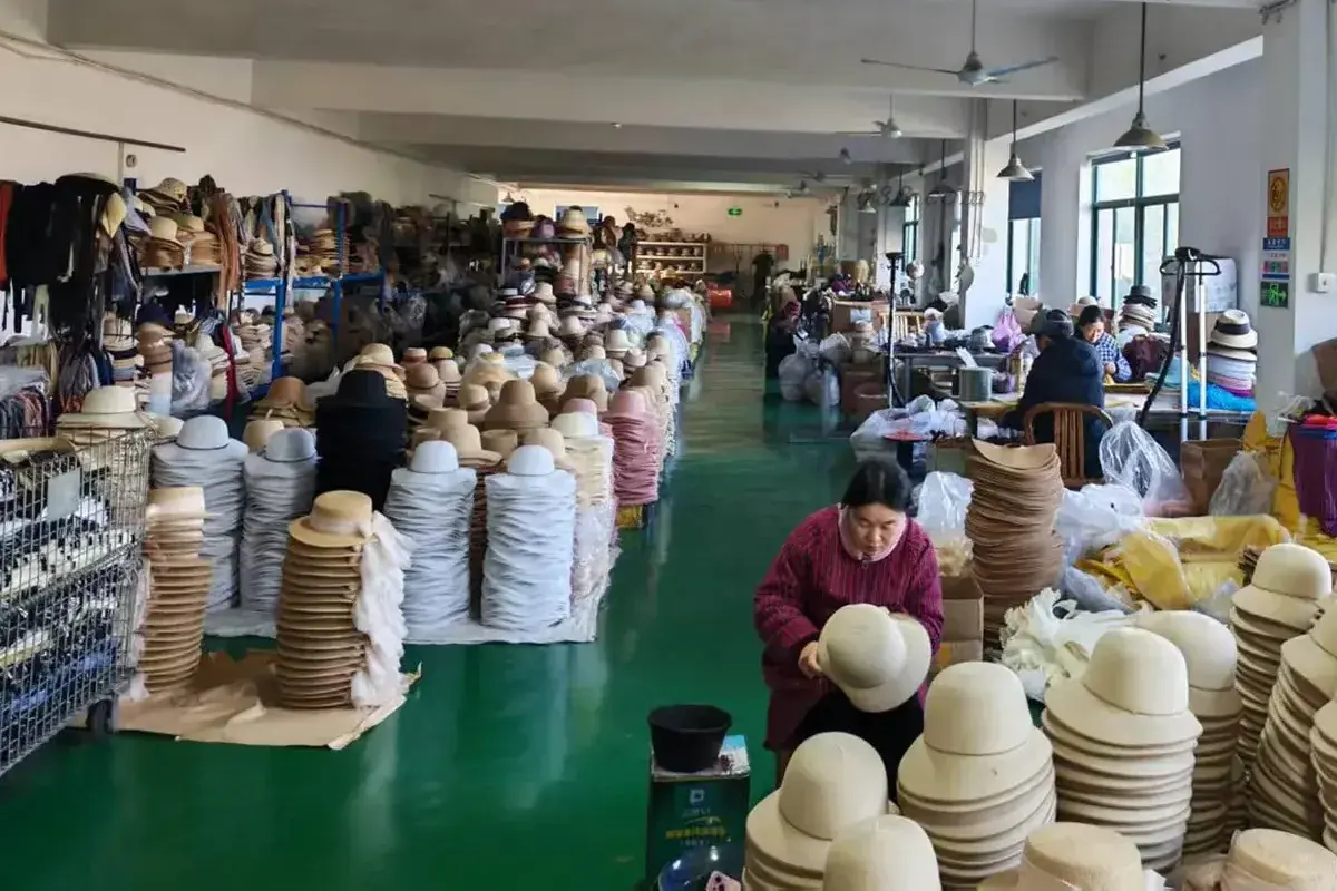 Workers developing and shaping straw hats across a busy factory workshop