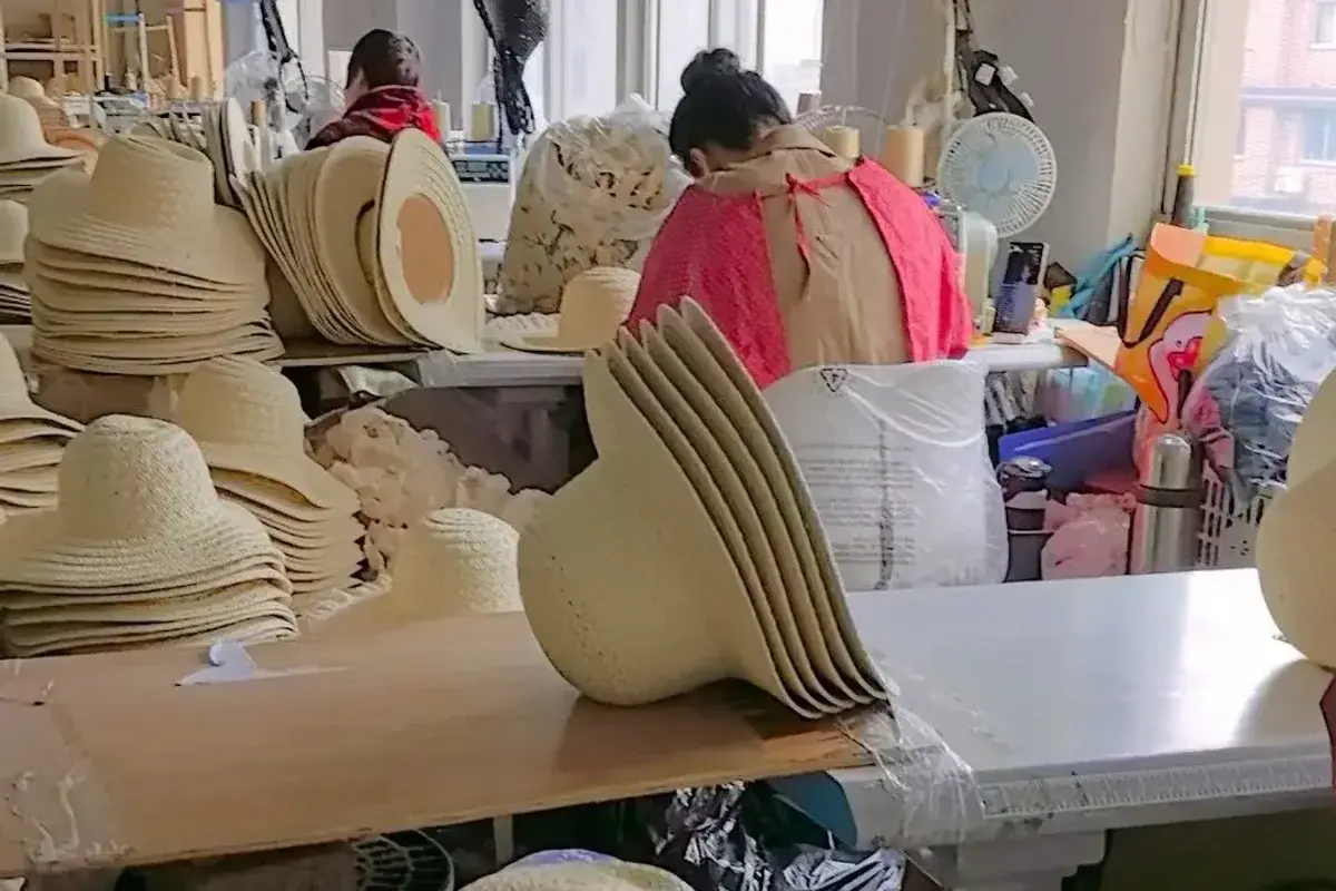 Factory worker handling wide-brim straw hat bodies during production