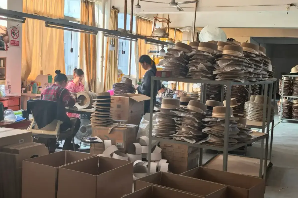 Factory packing area with finished straw hats, tissue protection, and open cartons