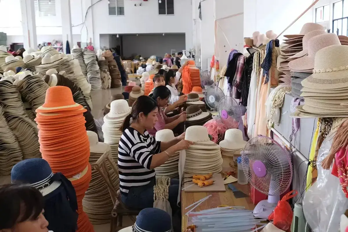 Factory workers assembling trims and finishing straw hats at production tables