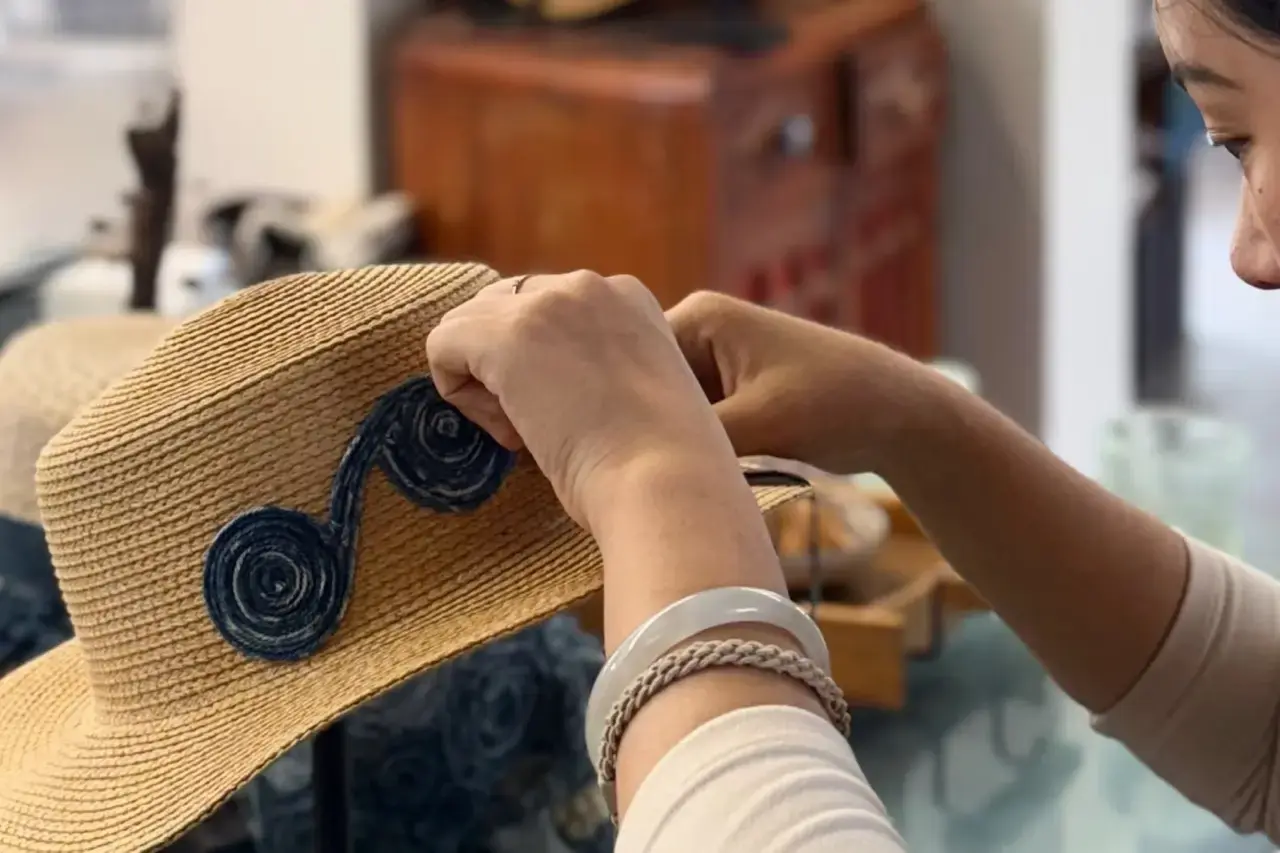Worker attaching decorative trim to a custom straw hat